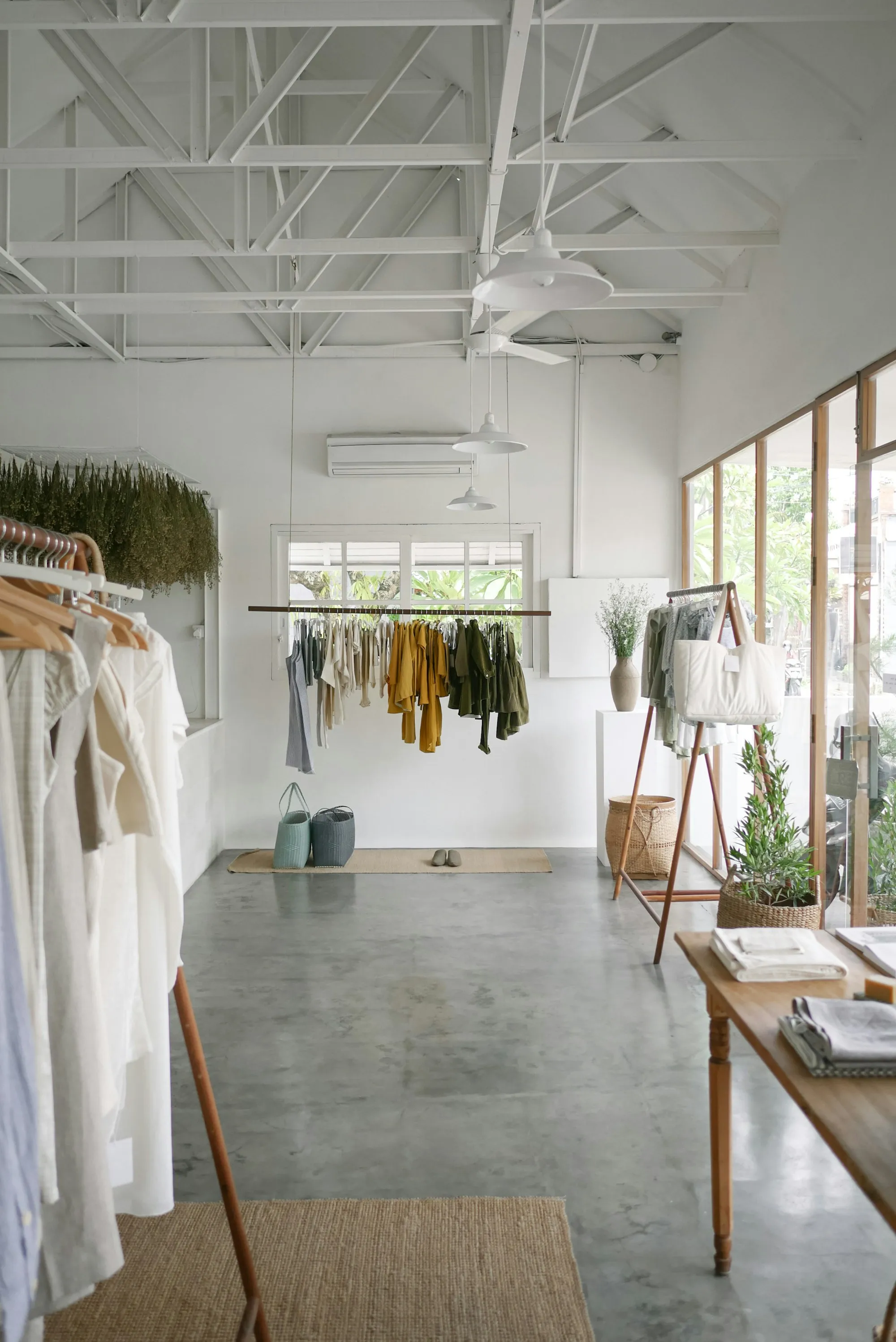 A bright small boutique interior with hanging garments, wooden fixtures, and plants.
