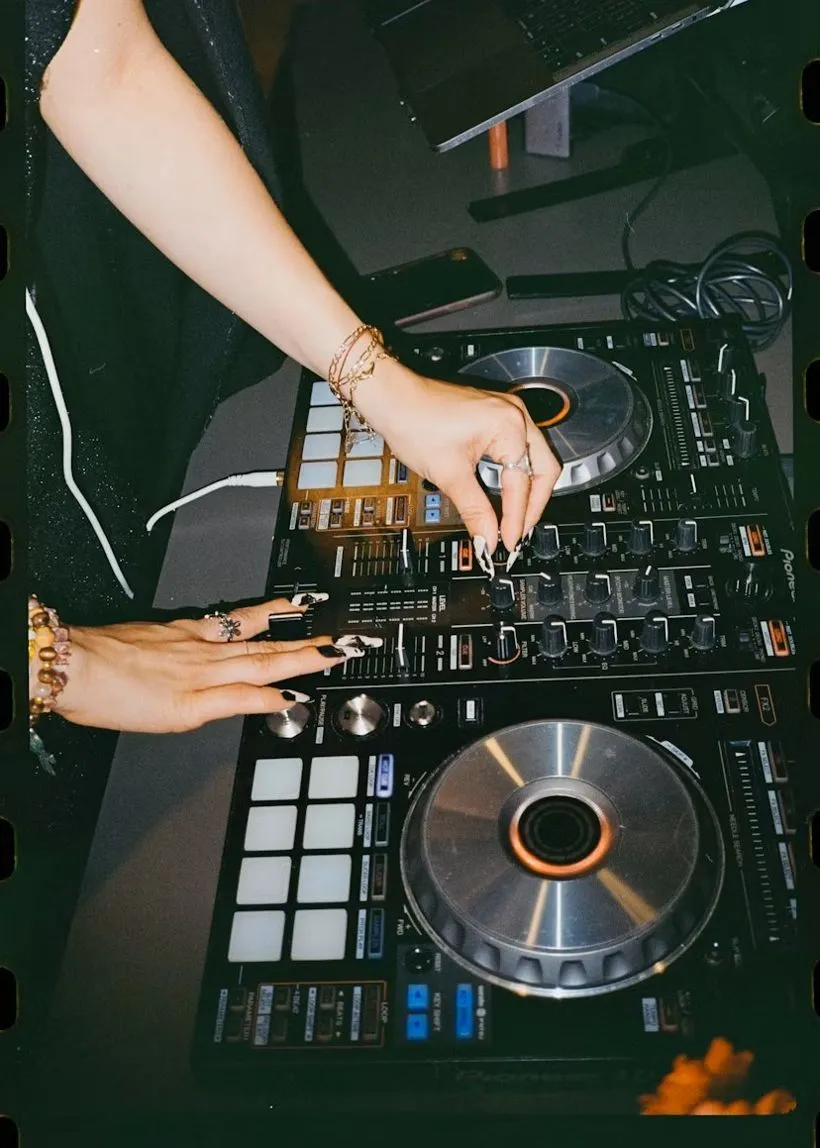 A DJ at the booth mid-set, headphones on, blue stage light overhead.