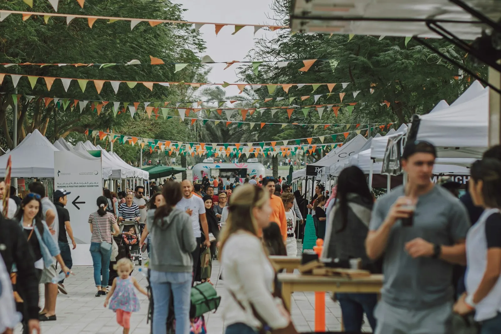 A daytime street market with bunting strung between trees, food-stall tents, and neighbours mingling. The kind of neighbourhood-scale local economy this page is for.